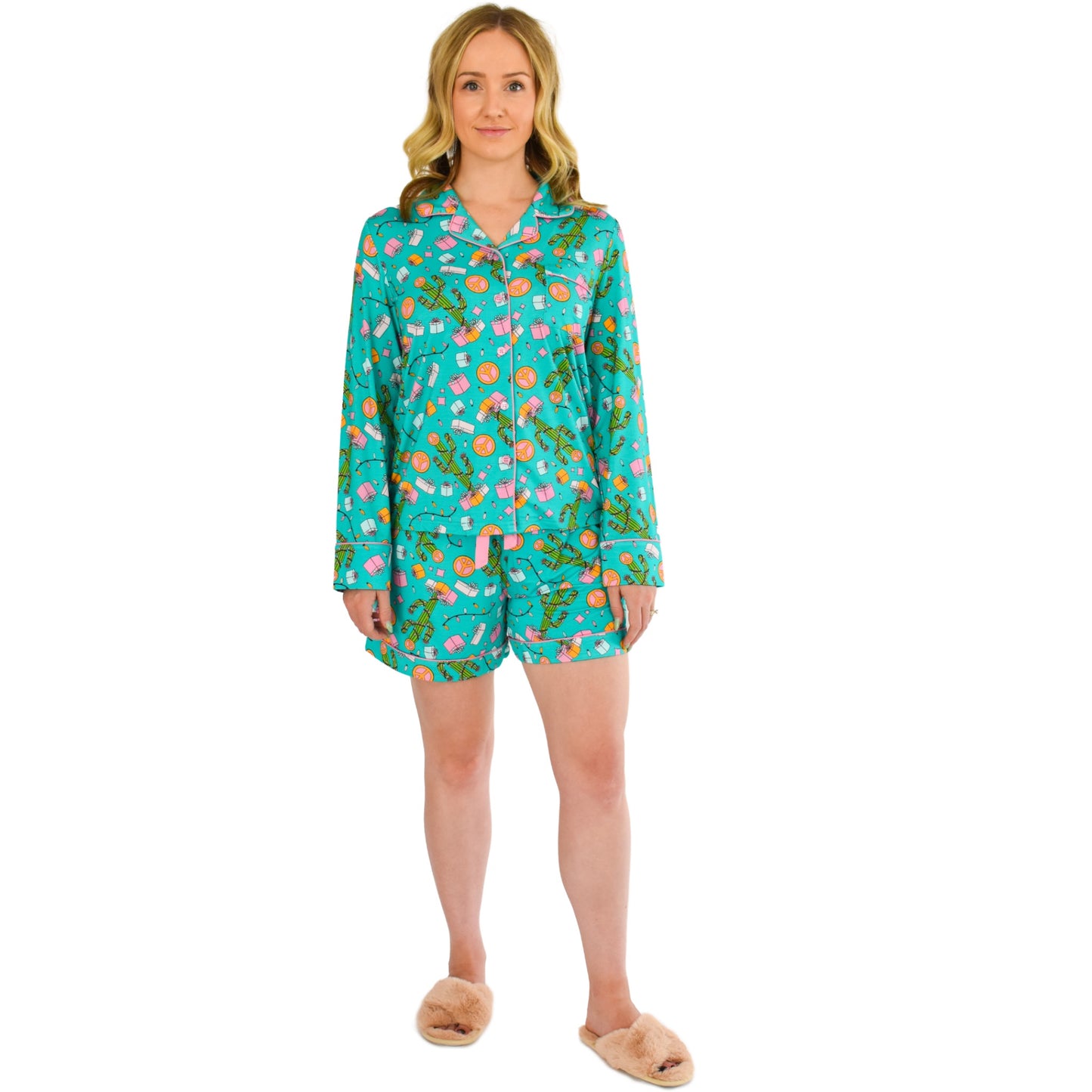 A girl wearing cozy bamboo pajamas by Cozy Ups. The pajamas have long sleeves and shorts, featuring a festive teal print adorned with cacti, string lights, and Christmas gifts. The comfortable and sustainable bamboo fabric adds an extra touch of luxury to the cozy holiday-themed sleepwear