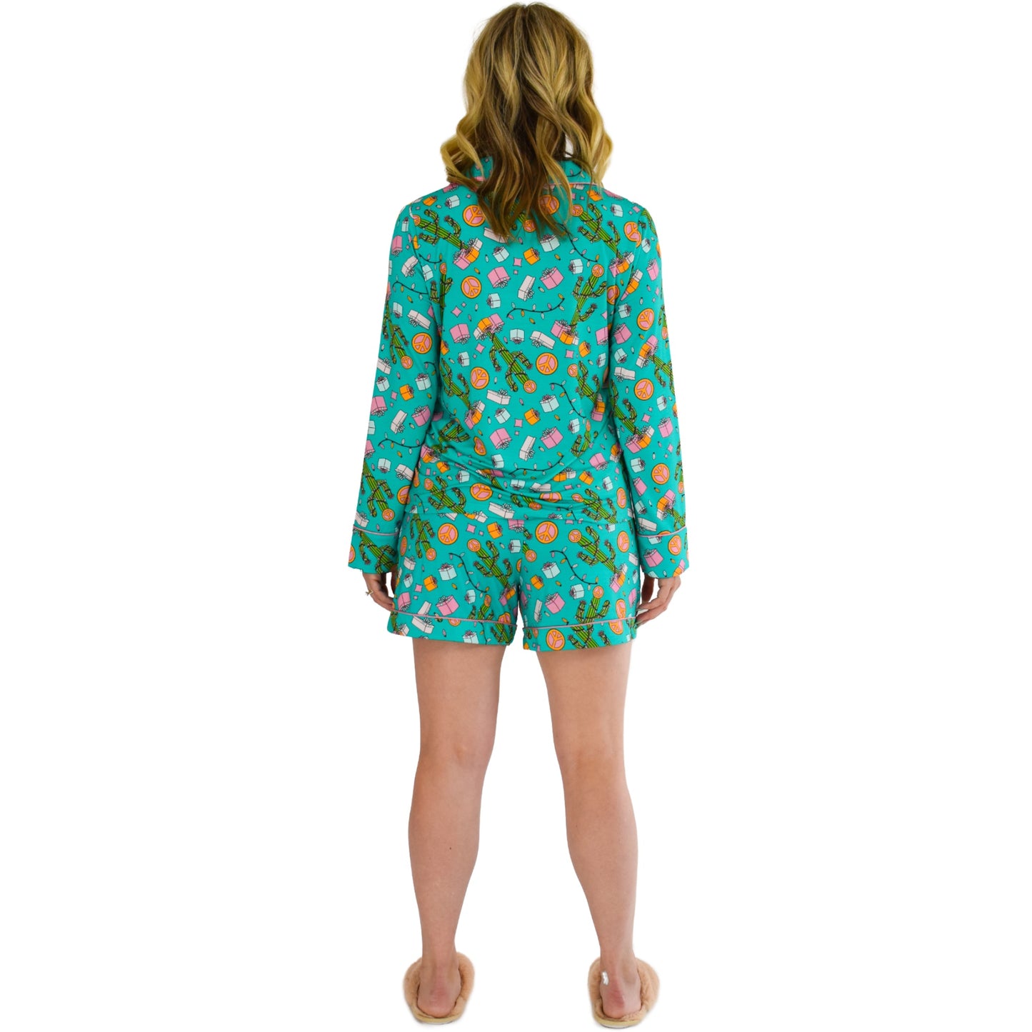 A girl wearing cozy bamboo pajamas by Cozy Ups. The pajamas have long sleeves and shorts, featuring a festive teal print adorned with cacti, string lights, and Christmas gifts. The comfortable and sustainable bamboo fabric adds an extra touch of luxury to the cozy holiday-themed sleepwear